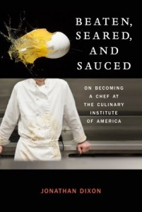 In the upper third a breaking egg shoots across a black background, in the lower two thirds a chef leans against the counter, shown from neck to waist