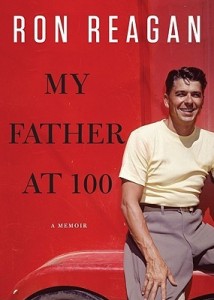 Against a red wall and a red car, a young Ronald Reagan leans casually, smiling and wearing a beige tee shirt with belted khakis